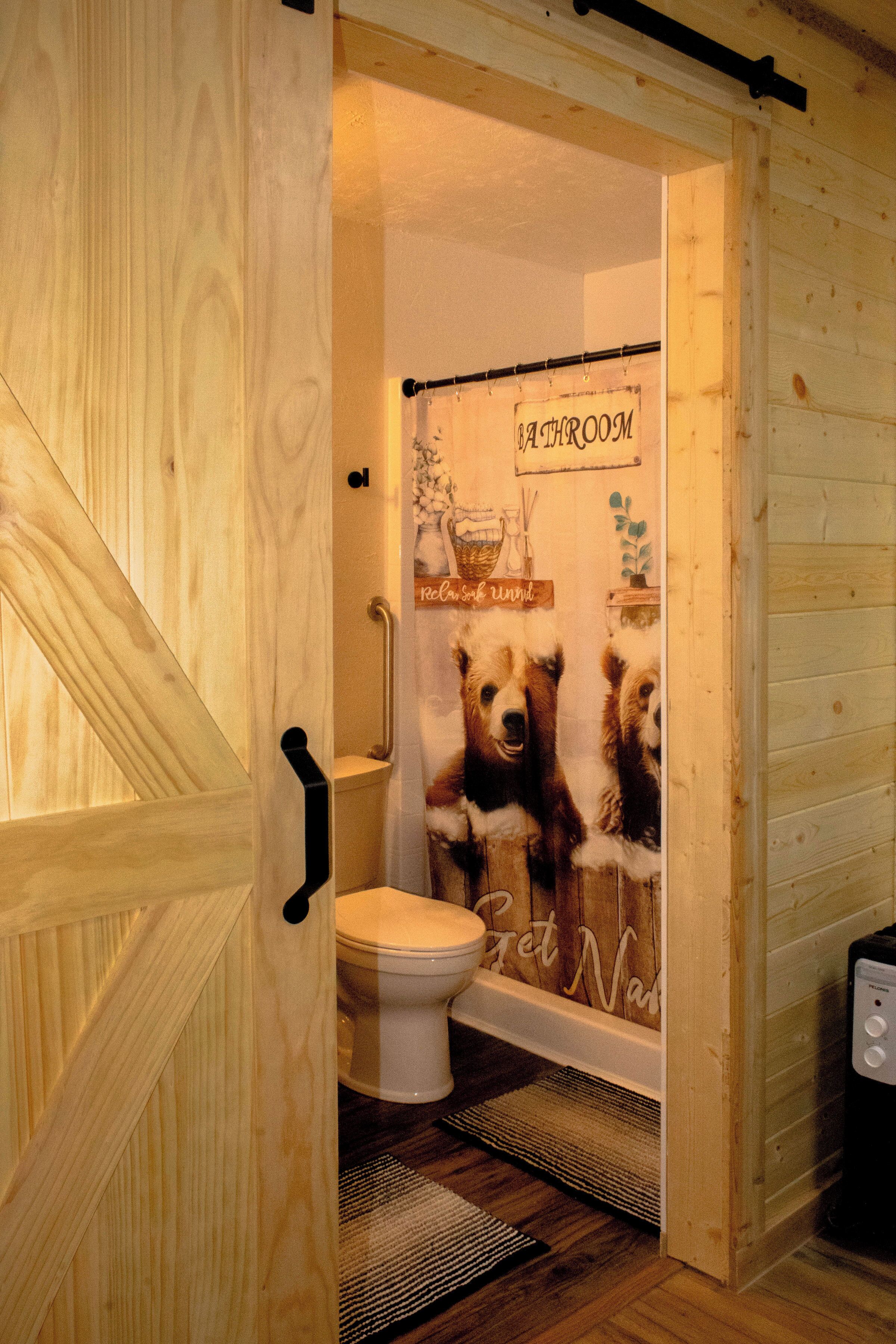 Une salle de bain en bois avec un rideau de douche orné d’un motif d’ours, des toilettes et un bidet.