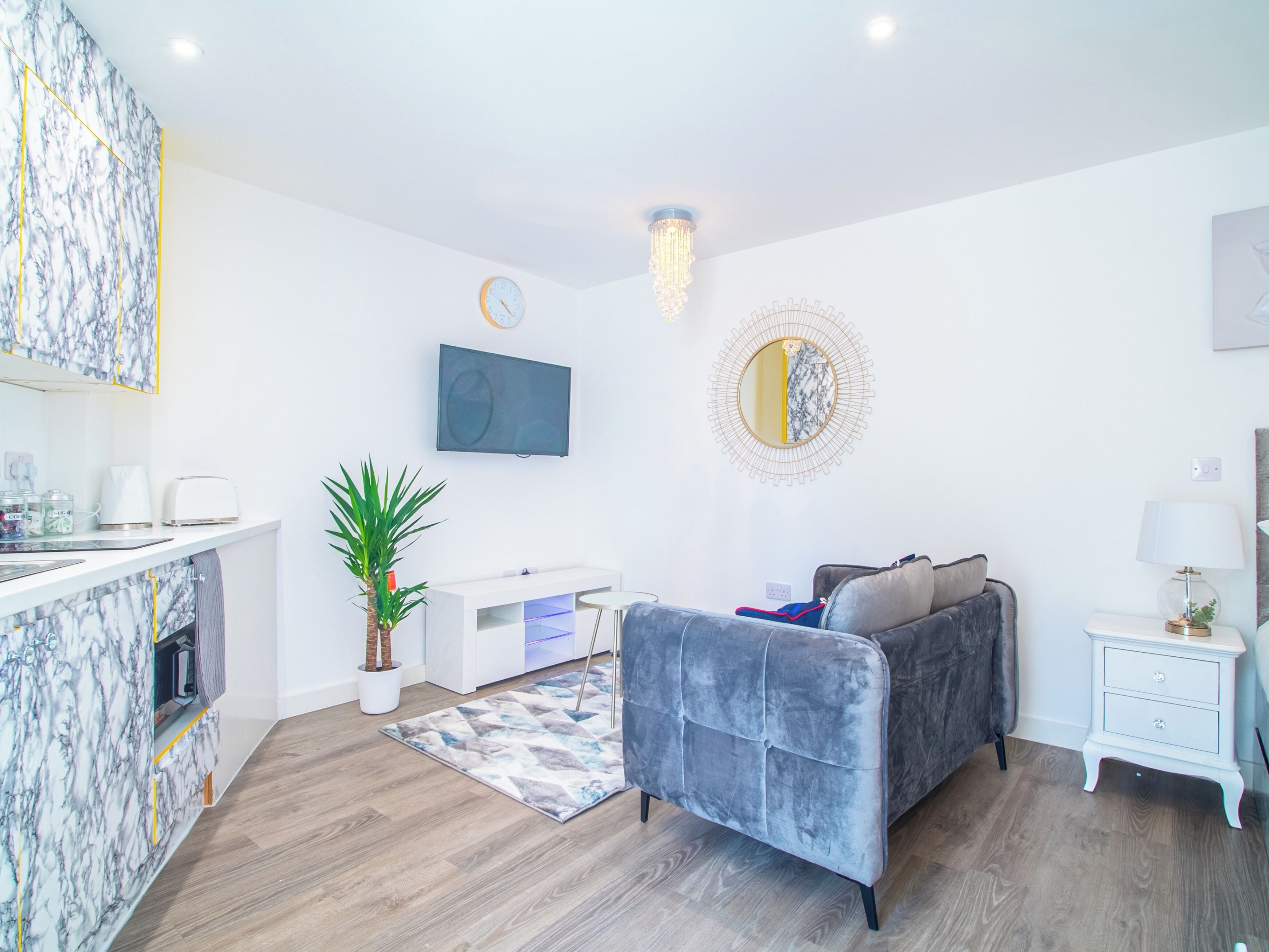 A modern living room with a grey sofa, a flat-screen TV, a decorative mirror, and a small side table.