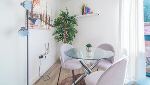 Un espace repas moderne avec une table en verre, deux chaises, une plante en pot et un tableau représentant un paysage urbain accroché au mur.