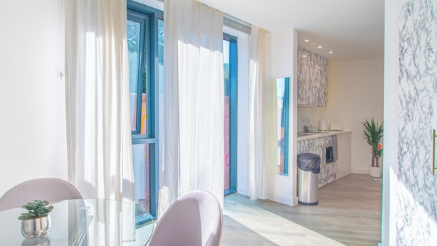 Un salon moderne avec une table en verre, un canapé et une vue sur la cuisine et le balcon.