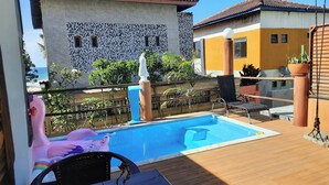 Une piscine avec une terrasse en bois, un flotteur en forme de flamant rose et une statue.