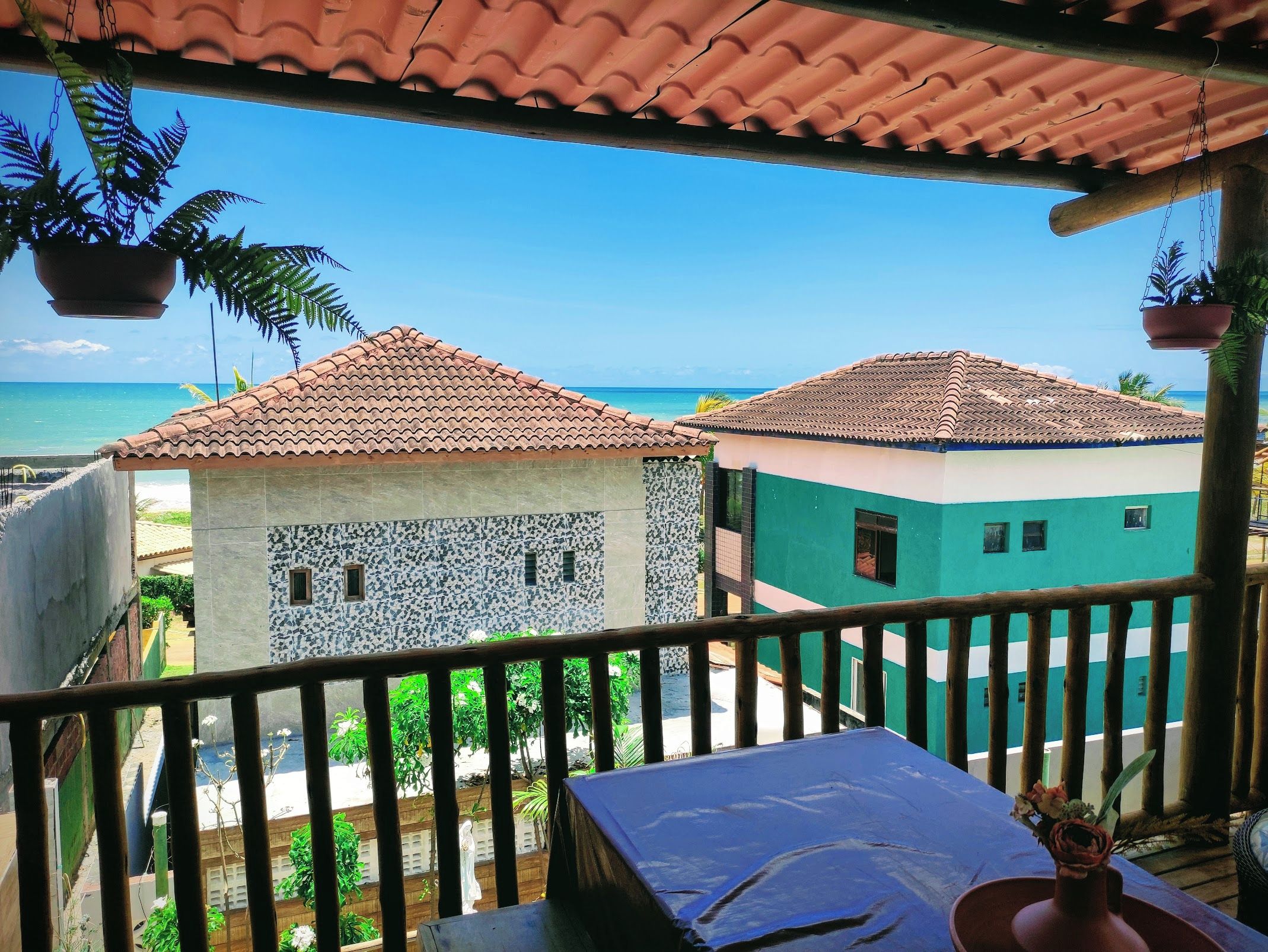 A balcony with a view of a beach and two buildings with tiled roofs.