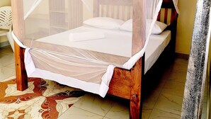 Un llit amb cortines mosseebrades de color blanc en una habitació amb parets grogues i un paviment amb motius.