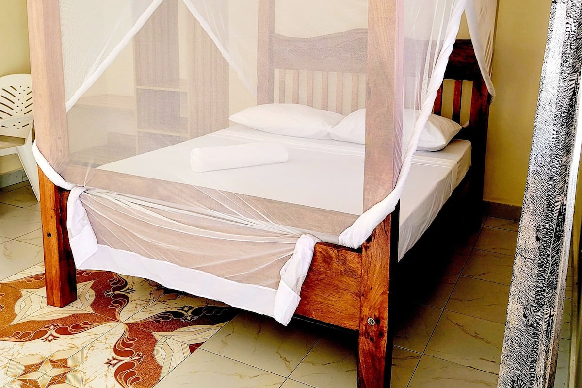 A four-poster bed with a white canopy in a room with yellow walls and a patterned floor.