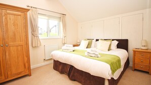 A bedroom with a large bed, wooden wardrobe, and a window with curtains. - Four bedroom holiday lodge with onsite watersports. (Saint Columb Major)