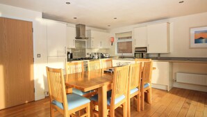 A modern kitchen with white cabinets, a wooden dining table with chairs, and a built-in oven. - Four bedroom holiday lodge with onsite watersports. (Saint Columb Major)