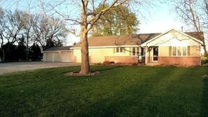 A single-story house with a garage, a front lawn, and a tree in the foreground.