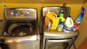 A front-loading stainless steel washer and dryer with detergent bottles on top.