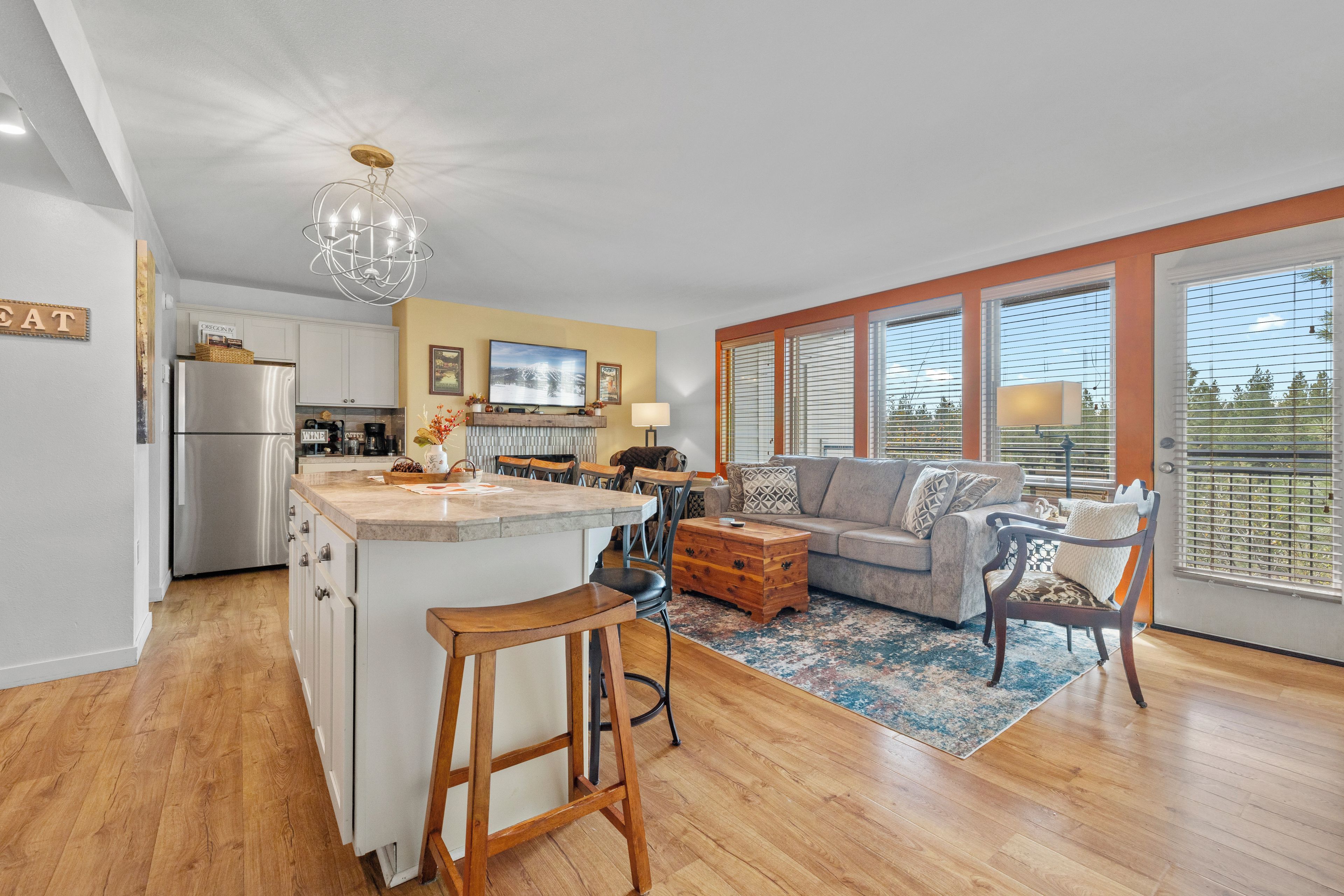 A modern kitchen with a central island, a dining area with a sofa and chairs, and large windows with blinds.