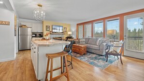 A modern kitchen with a central island, a dining area with a sofa and chairs, and large windows with blinds. - Mount Bachelor Ski Condo w/Hot Tub & Pool Sleeps 6 (Bend)