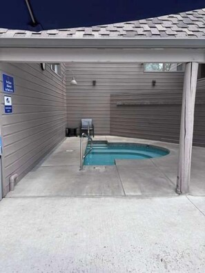 Een overdekt zwembadgedeelte met een betonnen vloer, een metalen zwemtrap en een blauw bord waarop staat dat er een douche is voor mensen met een handicap.