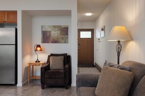 Un salon avec un canapé, un fauteuil, une lampe et un tableau accroché au mur.