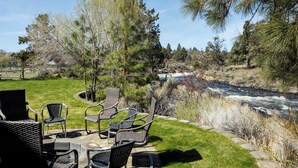 Un espace extérieur aménagé avec des chaises en osier et une table en pierre, offrant une vue sur une rivière et entouré d’arbres.