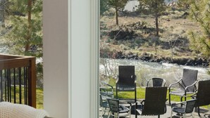 Une pièce dotée d’une grande fenêtre donnant sur un patio aménagé avec du mobilier d’extérieur et offrant une vue sur la rivière.