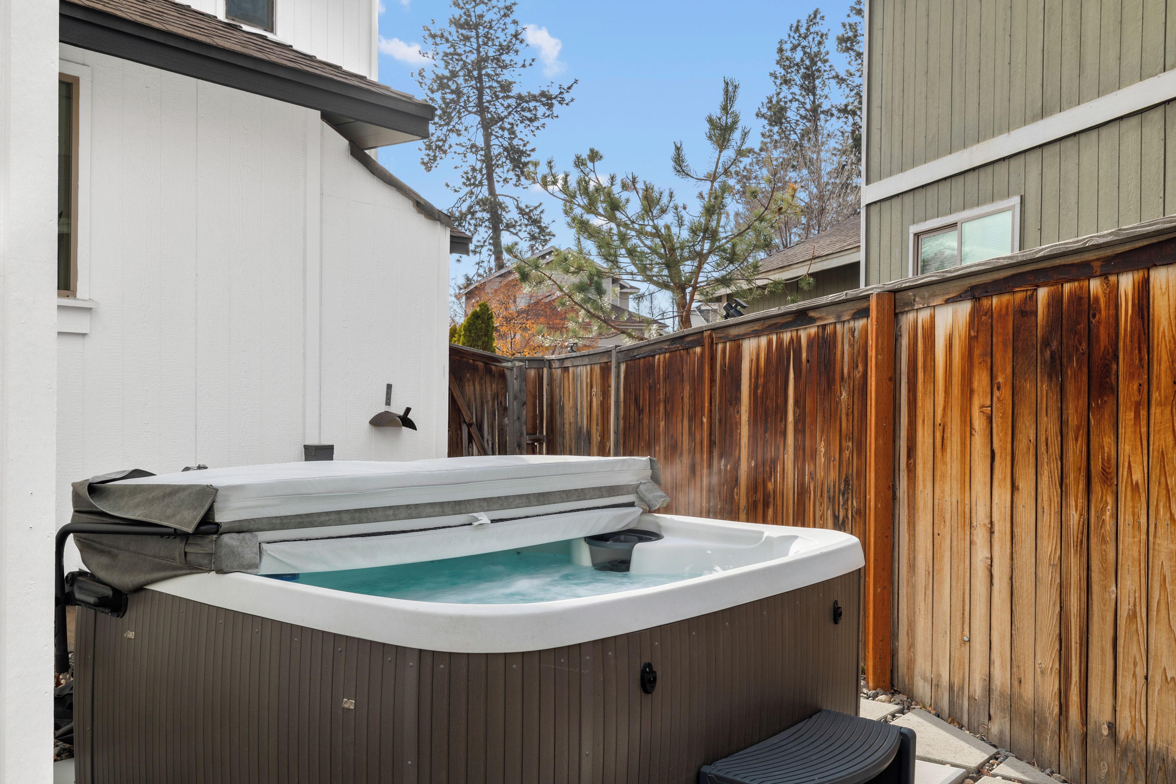 A hot tub in a backyard with a wooden fence and a house in the background.