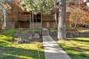 A two-story building with a stone facade, a front entrance with a metal gate, and a concrete pathway leading to the door.