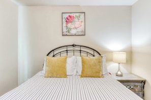 A neatly made bed with striped bedding and two pillows, a bedside lamp, and a floral artwork on the wall.