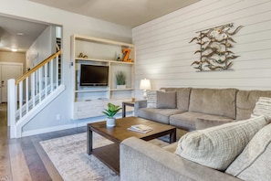 A modern living room with a staircase, a flat-screen TV, a sofa, and a decorative wall piece.