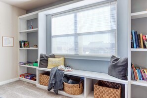 A cozy reading nook with a window, shelves with books and games, and storage baskets.
