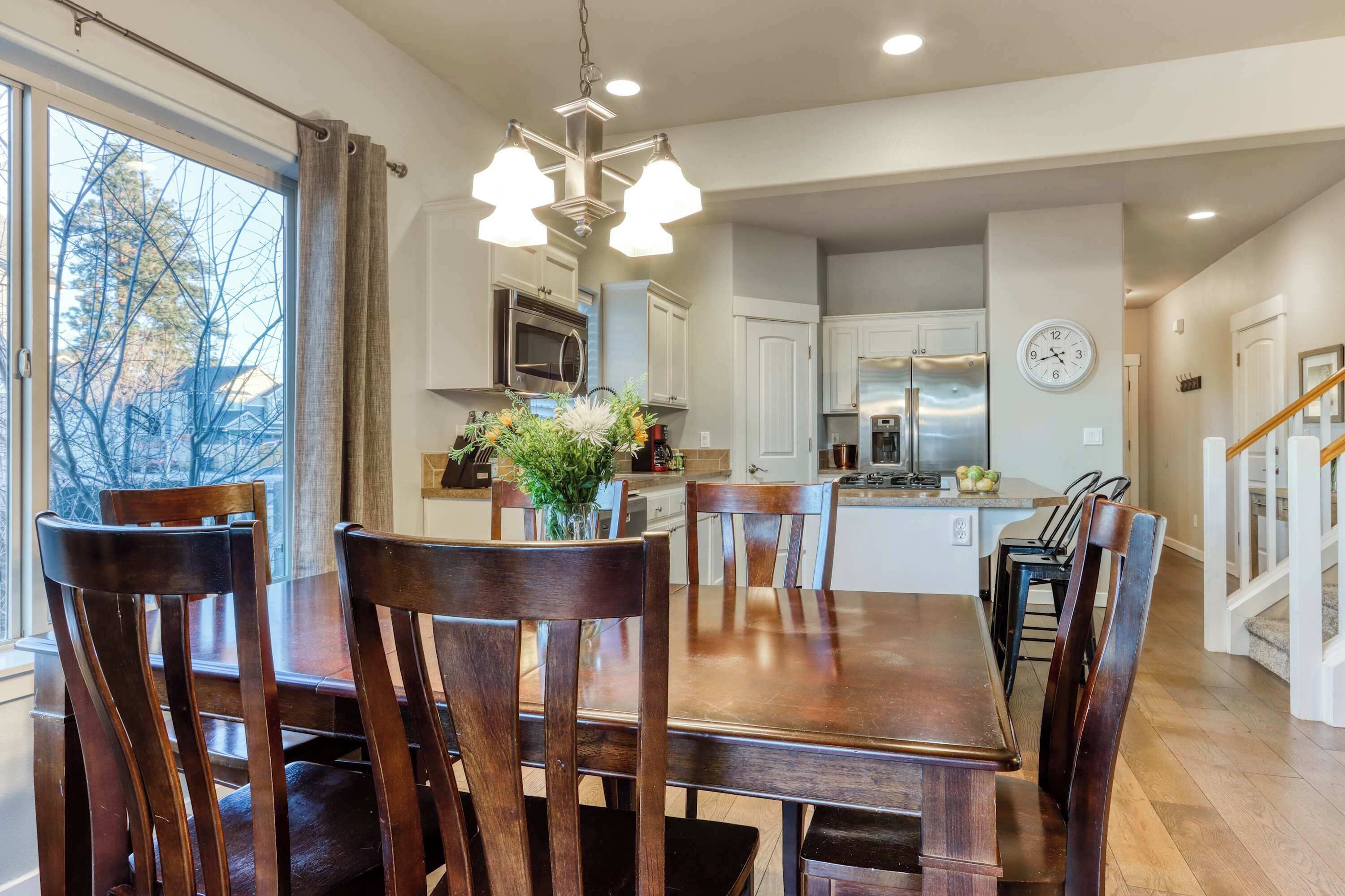 A dining area with a wooden table and chairs, a chandelier, and a view of the kitchen in the background.