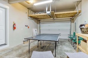 A garage with a ping pong table, green folding chairs, and a fire extinguisher.