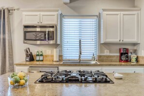 A kitchen with white cabinets, a stainless steel microwave, a gas stove, and a window with blinds. - 4BR Bend Home Near Mt Bachelor and River Trails (Bend)
