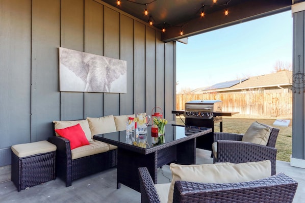 An outdoor patio with wicker furniture, a glass-top table, and a barbecue grill.