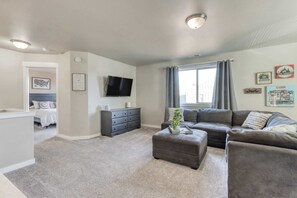 A living room with a grey sofa, ottoman, and a flat-screen TV on the wall.