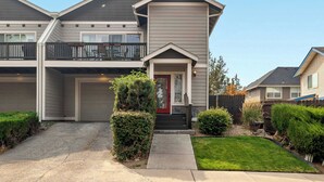 A two-story residential building with a garage, a front porch, and a small front yard with landscaping.
