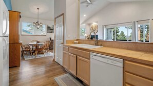 A modern kitchen with wooden cabinets, a dishwasher, a sink, and a dining area with chairs and a table.