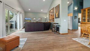 A spacious living area with a large sofa, a wooden dining table, and a kitchen in the background.