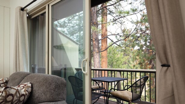 A balcony with a sofa and chairs, a glass door, and a view of trees. - Bend Condo Near Mt Bachelor with Hot Tub Sleeps 6 (Bend)