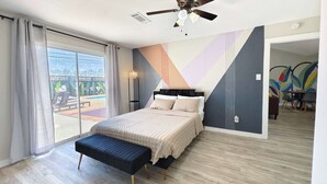 A bedroom with a bed, a bench, a ceiling fan, and a view of an outdoor area. - Sageview Cottage – 4 BDR w/ Pool, Pet Friendly! (Houston)