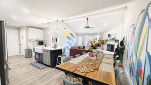 A modern kitchen with white cabinets, a central island, and a dining area with a wooden table and chairs. - Sageview Cottage – 4 BDR w/ Pool, Pet Friendly! (Houston)