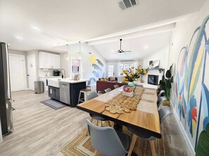 A modern kitchen with white cabinets, a central island, and a dining area with a wooden table and chairs. - Sageview Cottage – 4 BDR w/ Pool, Pet Friendly! (Houston)