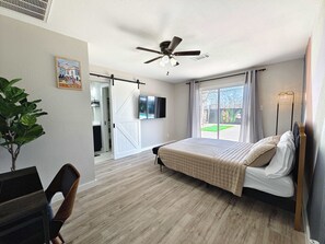 A bedroom with a bed, a ceiling fan, a TV, a sliding door, and a view of the outdoors. - Sageview Cottage – 4 BDR w/ Pool, Pet Friendly! (Houston)