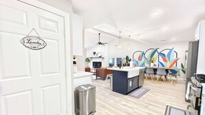 A modern kitchen with a central island, stainless steel appliances, and a dining area with colorful abstract wall art. - Sageview Cottage – 4 BDR w/ Pool, Pet Friendly! (Houston)