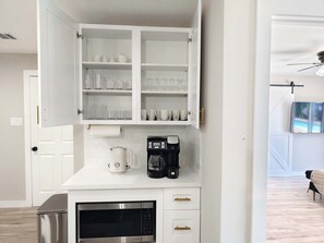 A kitchen with a white cabinet containing glassware and a coffee maker. - Sageview Cottage – 4 BDR w/ Pool, Pet Friendly! (Houston)