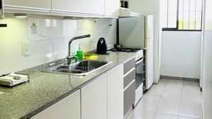 Una cocina moderna con armarios blancos, encimera de granito, horno empotrado y ventana con persianas.