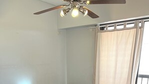 Una habitación con dos camas, suelo de madera, ventilador de techo y ventana con cortinas.