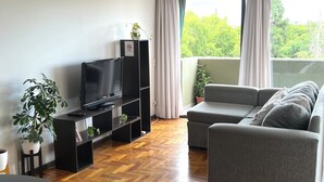 Una sala moderna con un sofá gris, un mueble de entretenimiento negro y un suelo de parqué de madera.