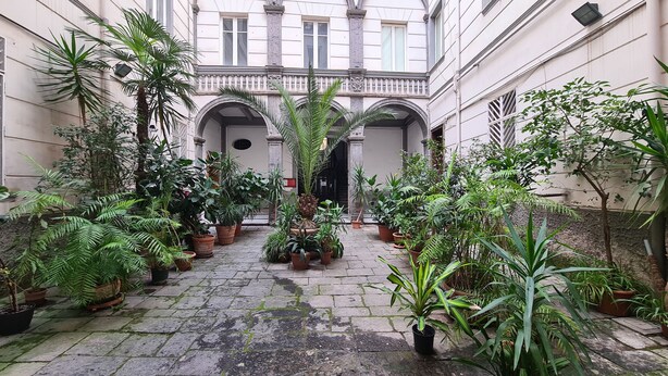 A courtyard with potted plants and a central archway. - Palazzo il Convento (Naples)