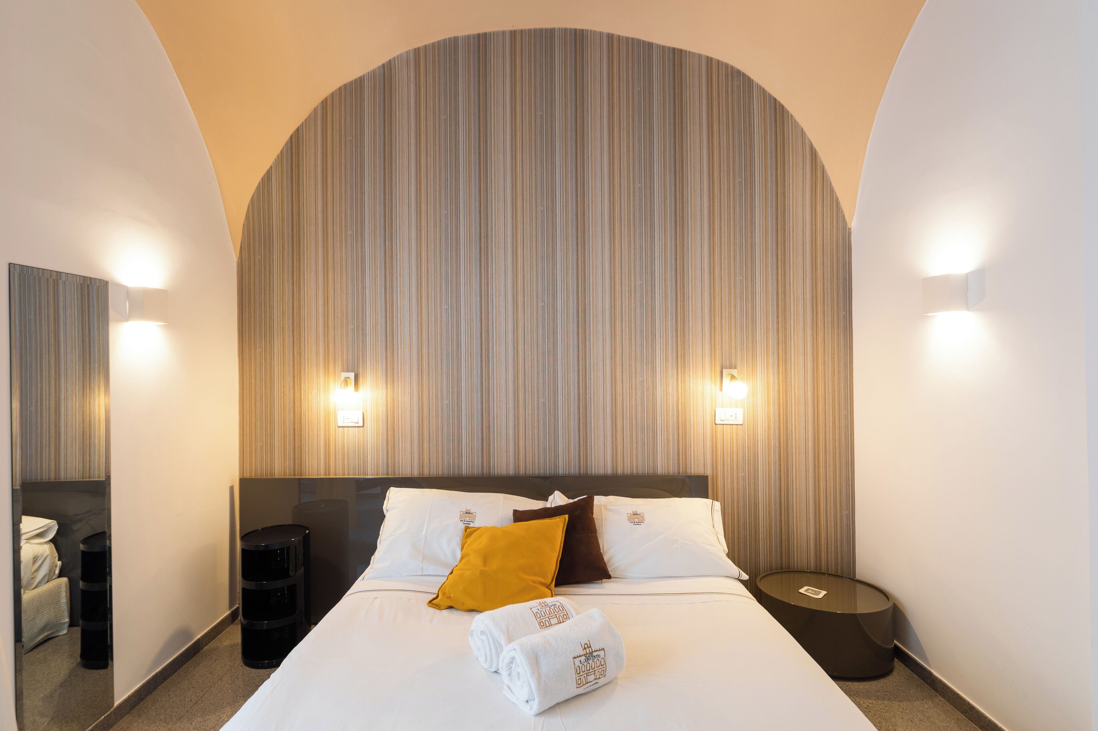 A hotel room with a large bed, a mirror, and two wall-mounted lights.
