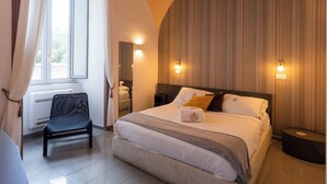 A hotel room with a bed, a chair, a bedside table, and a window with curtains. - Palazzo il Convento (Naples)