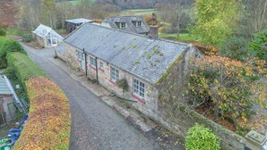 A stone building with a sloped roof, a gravel driveway, and a view of a hilly landscape. - Keeper's Cottage - North East Escapes  (Stocksfield)