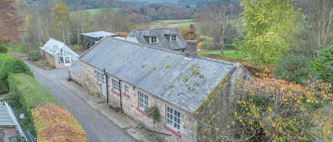 A stone building with a sloped roof, a gravel driveway, and a view of a hilly landscape.