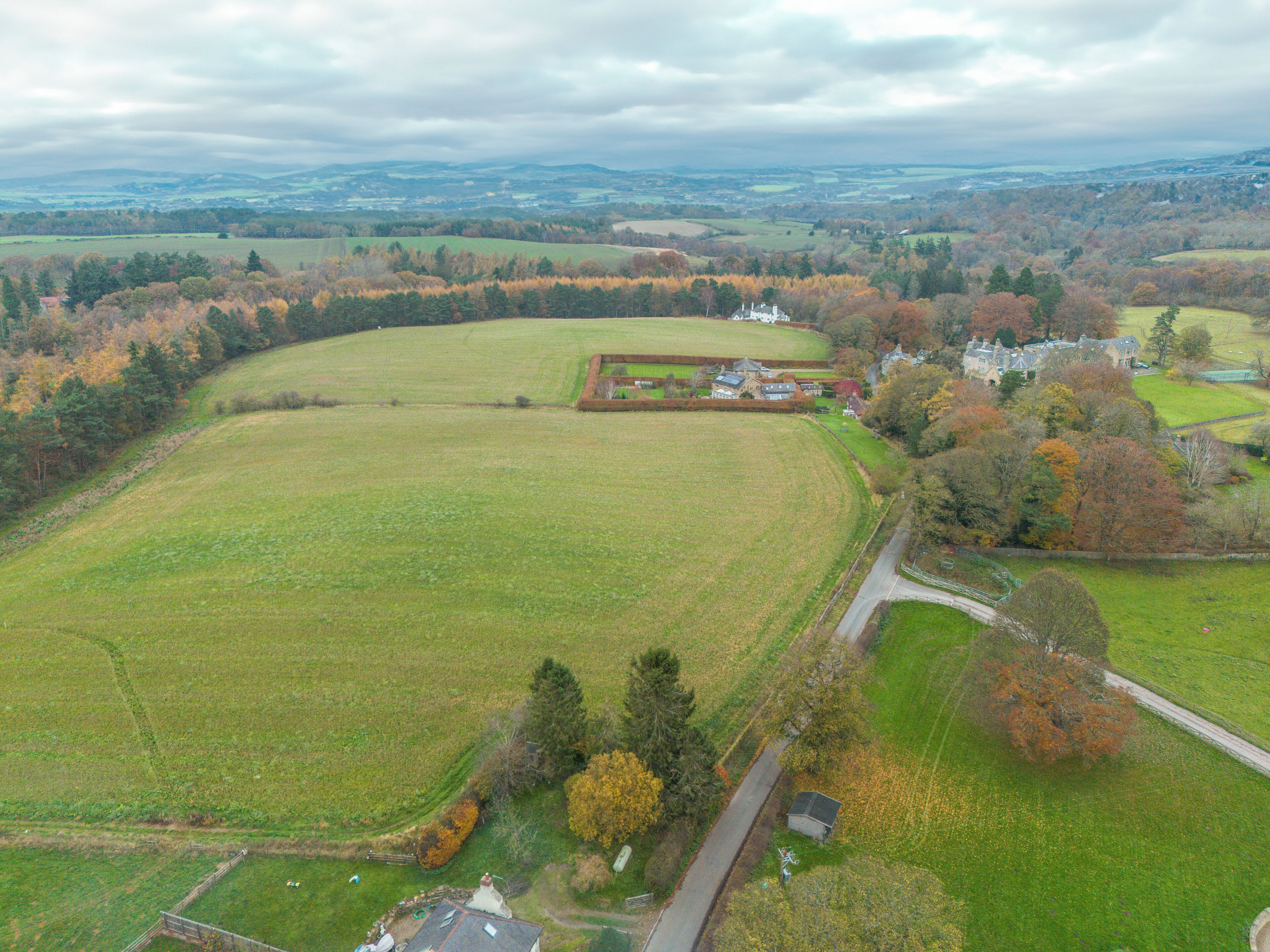 An aerial view of a rural property with a large open field, a small house, and a larger estate with multiple buildings.