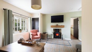 A living room with a fireplace, a television mounted on the wall, a wooden table, and a comfortable chair. - Keeper's Cottage - North East Escapes  (Stocksfield)