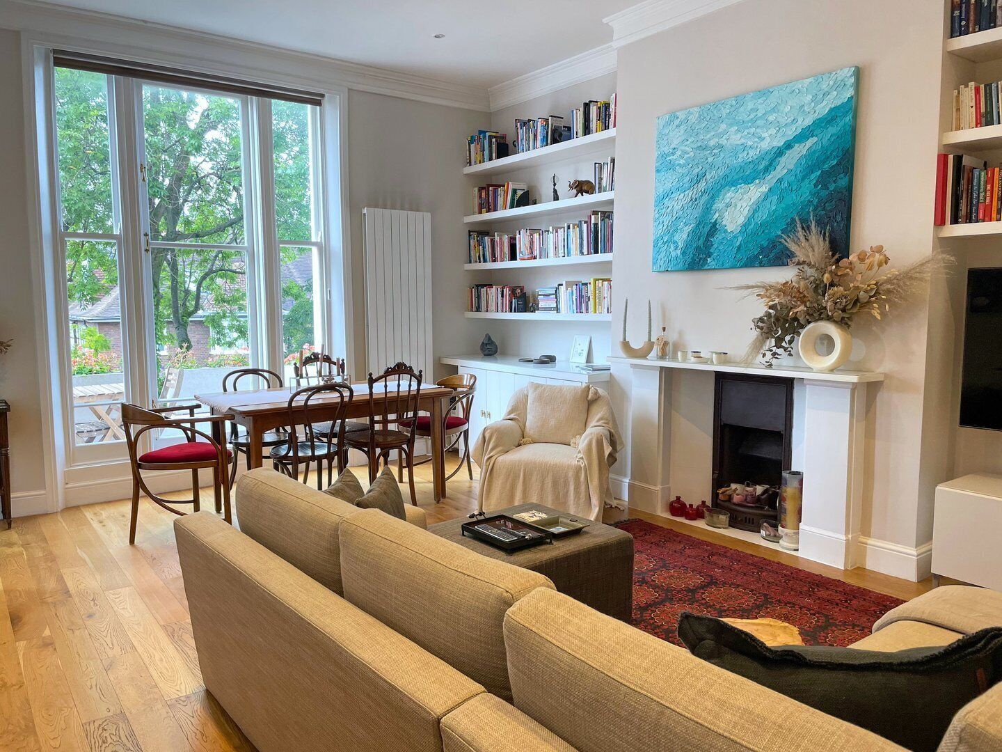 A living room with a fireplace, bookshelves, a dining area, and a large window.