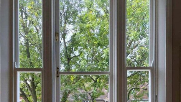 A room with a large window overlooking a residential area, a wooden table, and a chair.